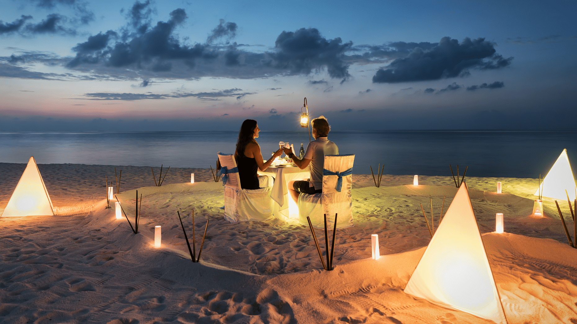Honeymooners on the beach surrounded by candles, sitting at a romantic table